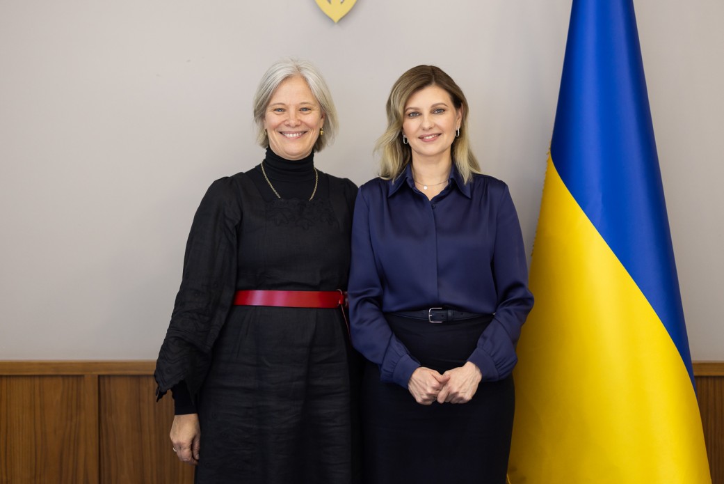 на фото Перша леді Олена Зеленська та Маріанна Ворд стоять біля Прапора України 