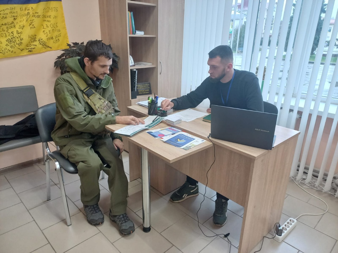 Двоє чоловіків сидять за робочим столом. На столі інформаційні матеріали