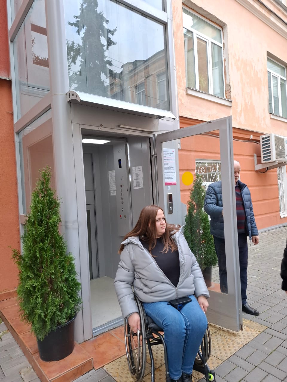 Дівчина в кріслі колісному біля входу до зовнішнього ліфта