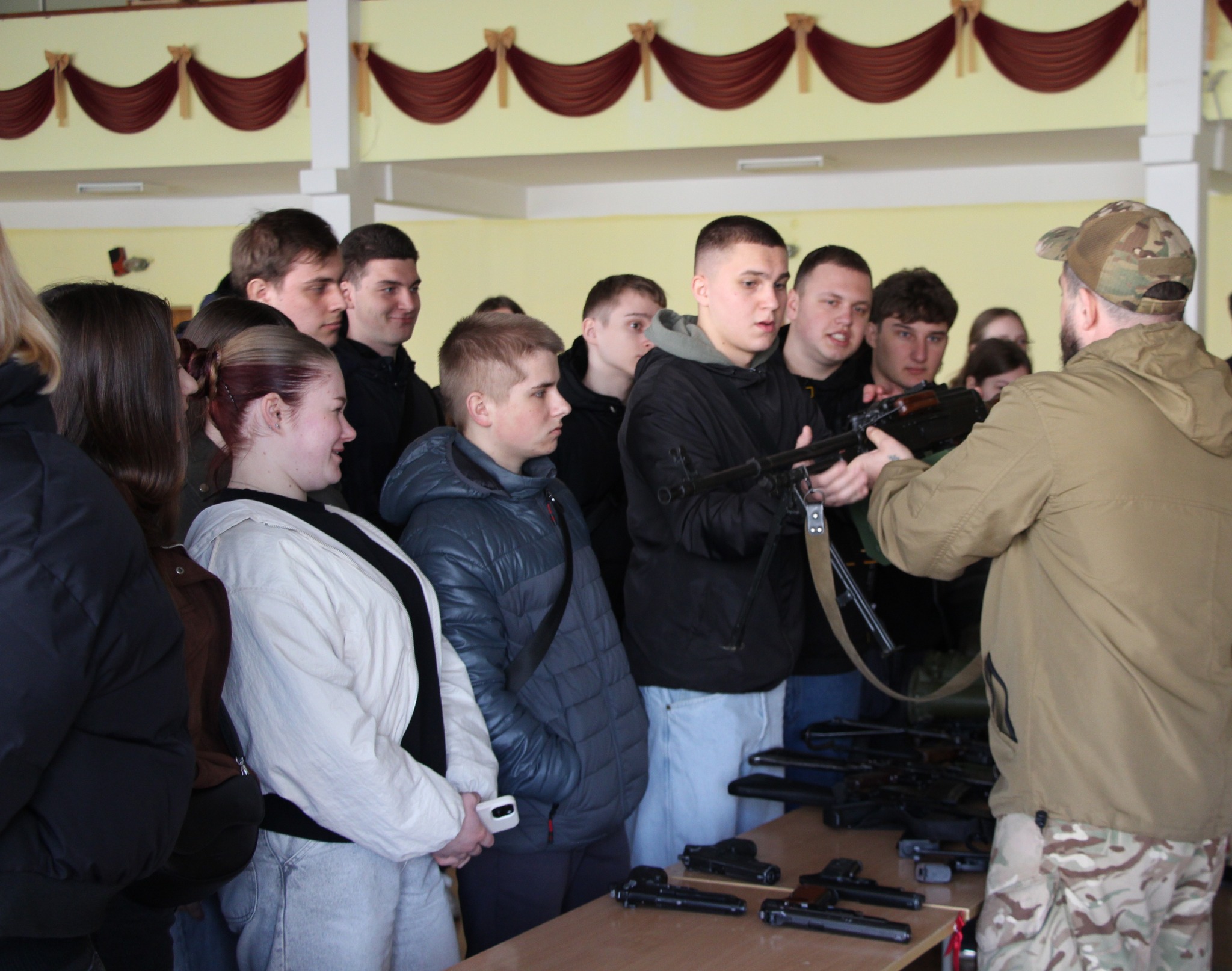 Група студентів стоїть напроти інструктора, який тримає навчальну зброю