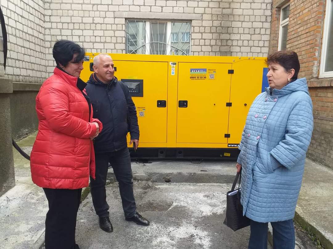 Дві жінки і чоловік спілкуються на вулиці біля будівлі лікарні