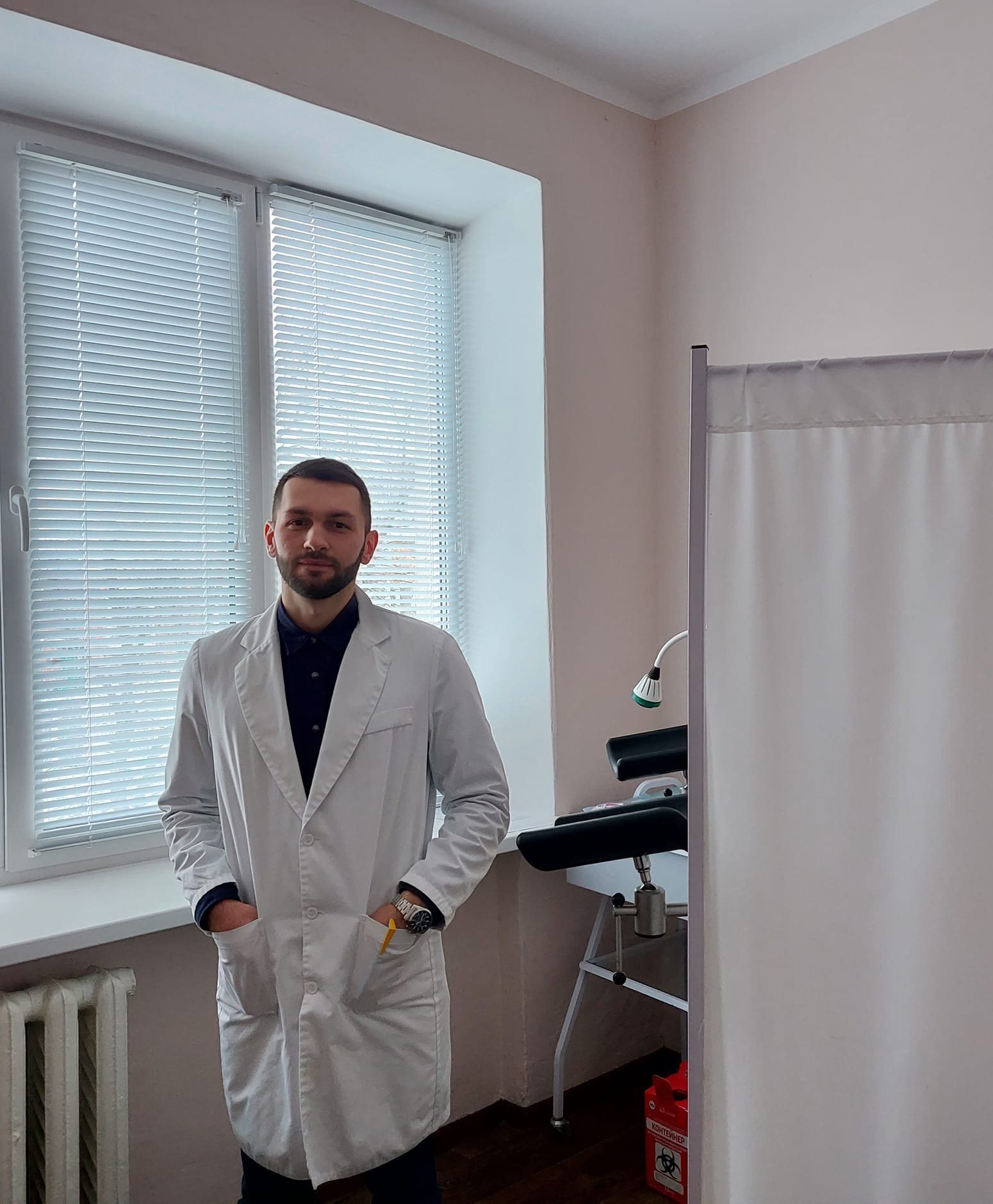 Чоловік у лабораторному халаті перед білою заслінкою.