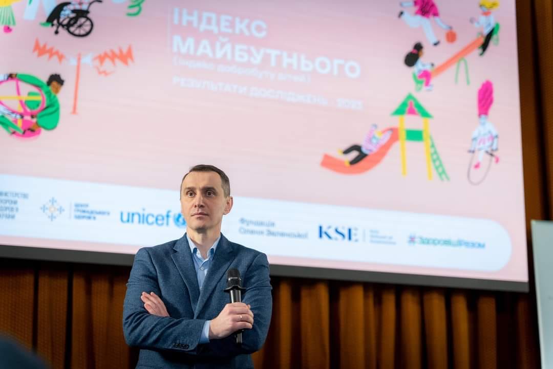 Чоловік у костюмі стоїть перед трибуною з мікрофоном.