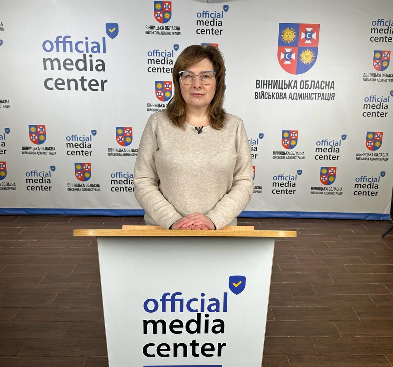 Жінка стоїть за кафедрою перед таблом з написом "Офіційний медіа-центр".