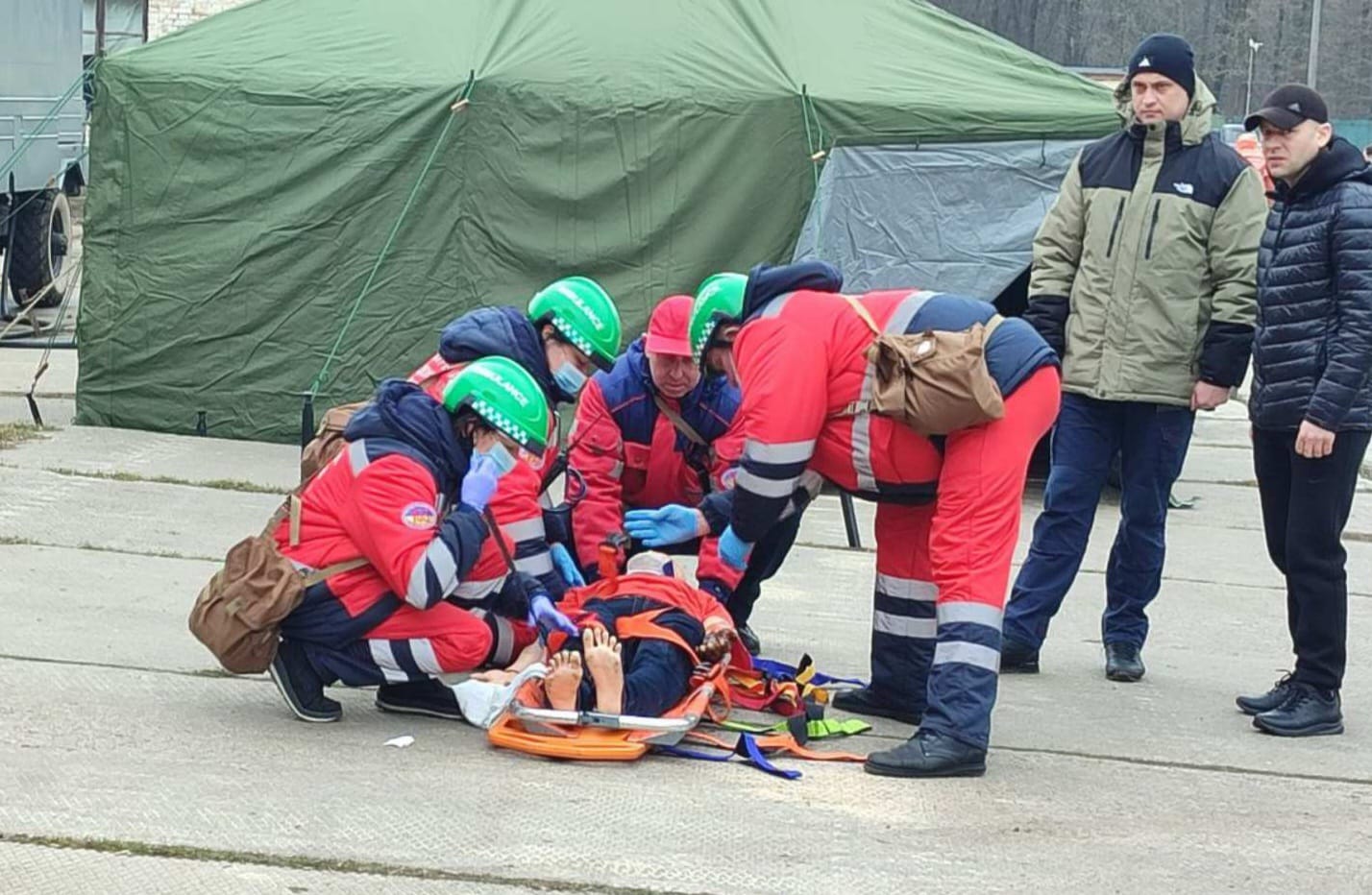 Група людей у червоній формі допомагає чоловікові на ношах.