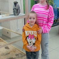 двоє дівчаток стоять біля клітки з мавпочкою