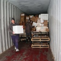 Двоє чоловіків вивозять з вантажного автомобіля коробки з гуманітарною допомогою