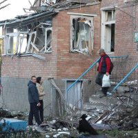 люди стоять біля пошкодженого будинку