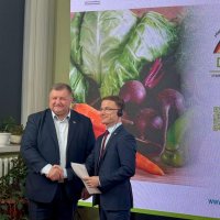 Двоє чоловіків у залі стискають один одному руки, позаду них банер 