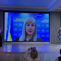 Великий монітор на сцені. Жінка доповідає у режимі відеоконференції 